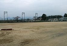 周囲に林や建物に囲まれた広々とした町営球技場の写真