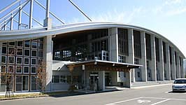 手前に駐車場が整備され、屋根がなだらかな湾曲した造りとなっている総合体育館の建物外観の写真